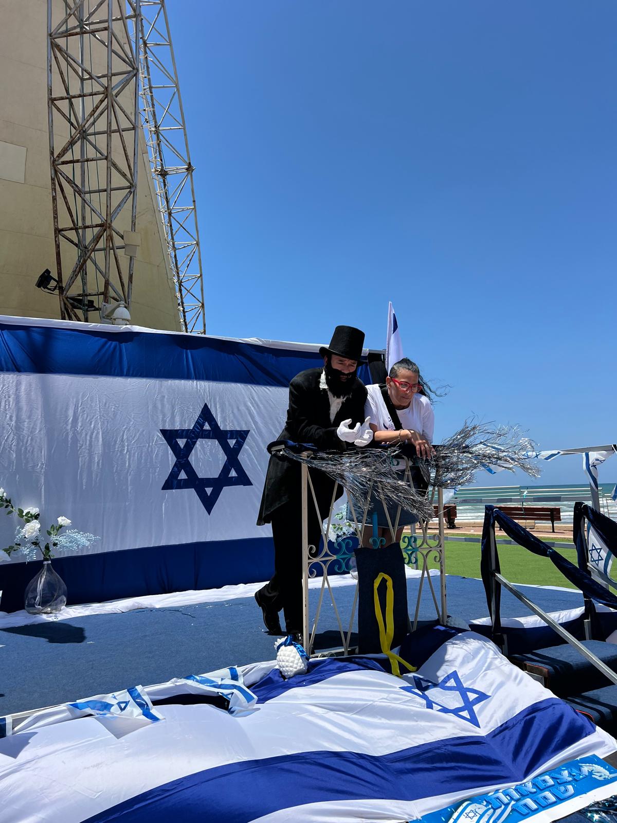 במה ועליה מרפסת בה ניצב שחקן המגלם את חוזה המדינה - בנימין זאב הרצל 